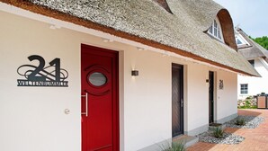 Un edificio con puerta roja, un cartel con el número 21 y techo de paja.