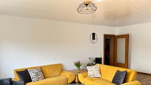 Un salon avec deux canapés jaunes, une table basse en verre et une horloge murale.