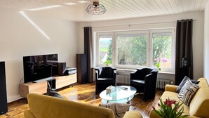 Un salon comprenant un téléviseur, un canapé, des fauteuils et une table basse en verre.