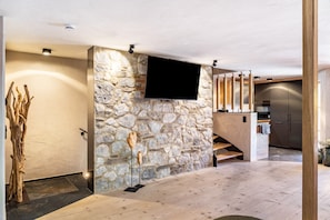A modern interior with a stone wall, a mounted TV, a wooden staircase, and a kitchen area. - Chalet 'Zur Auszeit' with Mountain View, Private Terrace and Wi-Fi (Mittenwald)