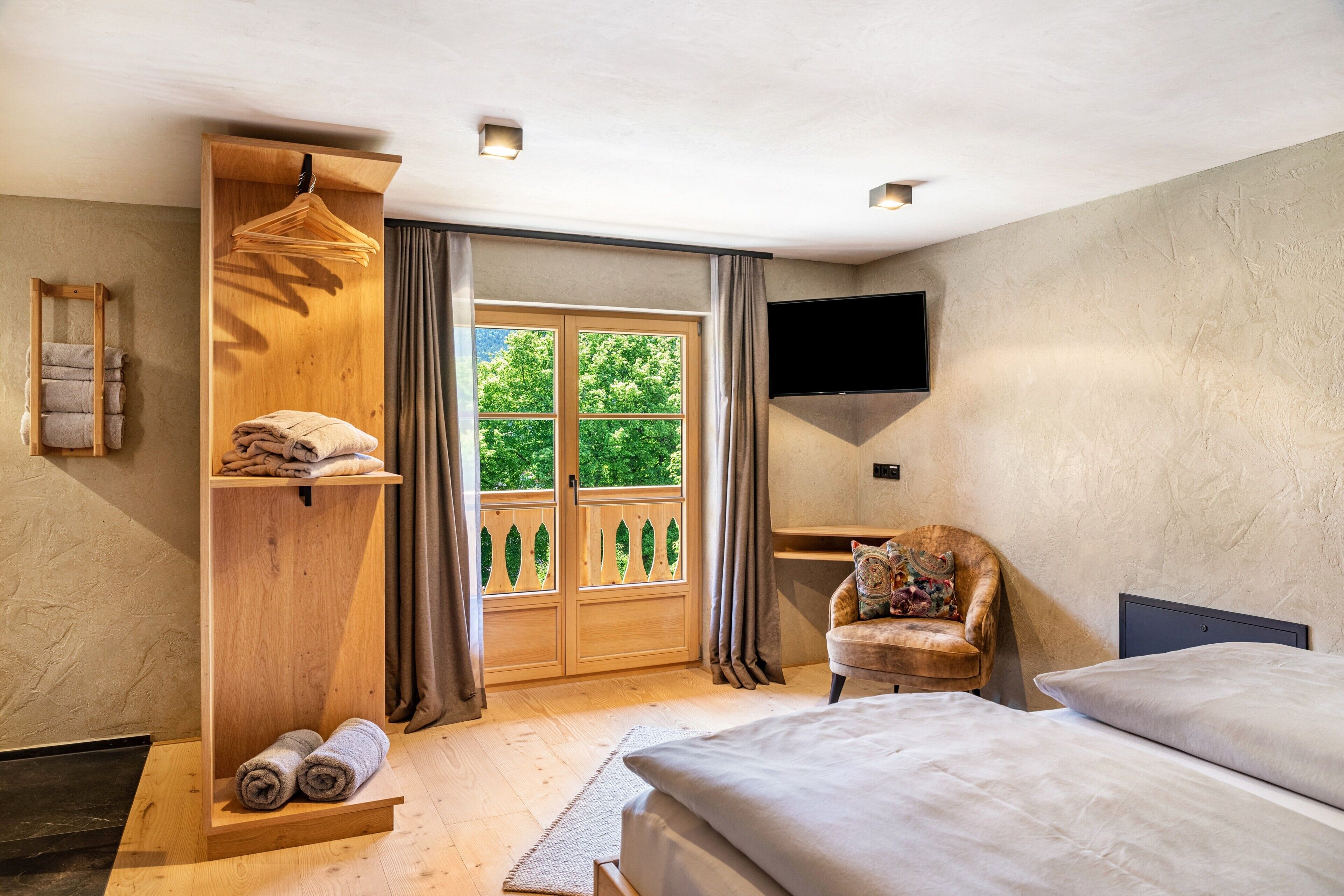 Une chambre à coucher avec un lit, une étagère en bois avec des serviettes, une chaise, un téléviseur et une fenêtre avec des rideaux.