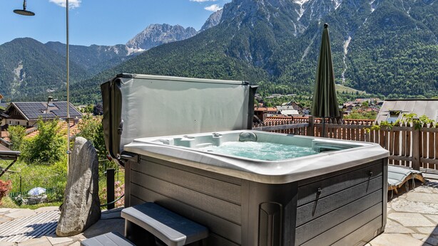 Un bain à remous avec vue sur les montagnes, une terrasse en bois et un banc en pierre.