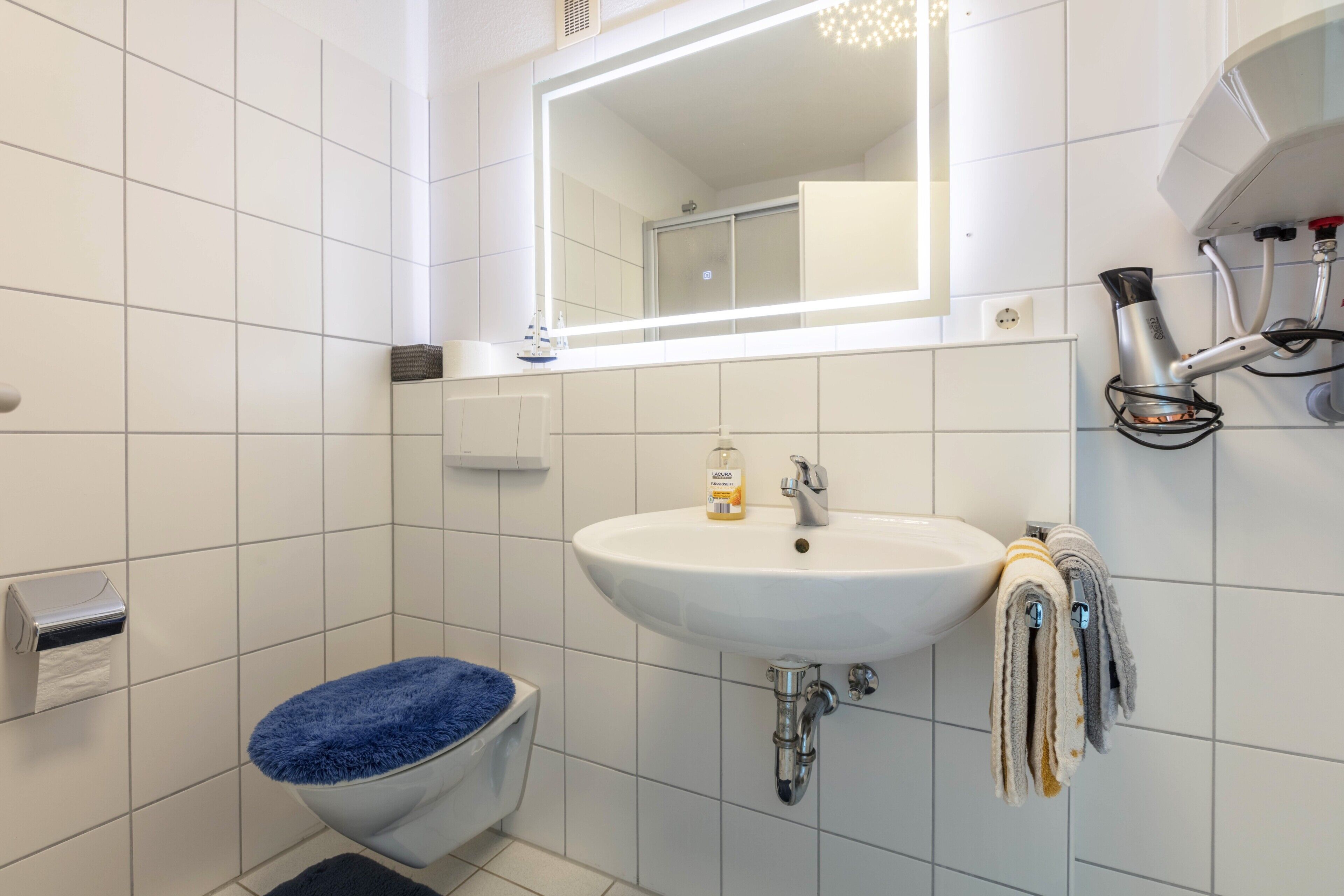 Een badkamer met een wit wastafel, een spiegel, een blauwe toiletbril en een handdoekhouder.
