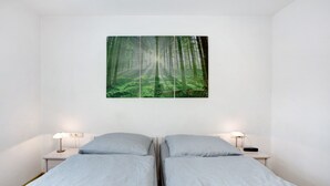 A bedroom with two beds, a forest-themed wall art, bedside lamps, and a white wall. - Apartment Ahorn with Private Terrace and Wi-Fi (Waldshut-Tiengen)