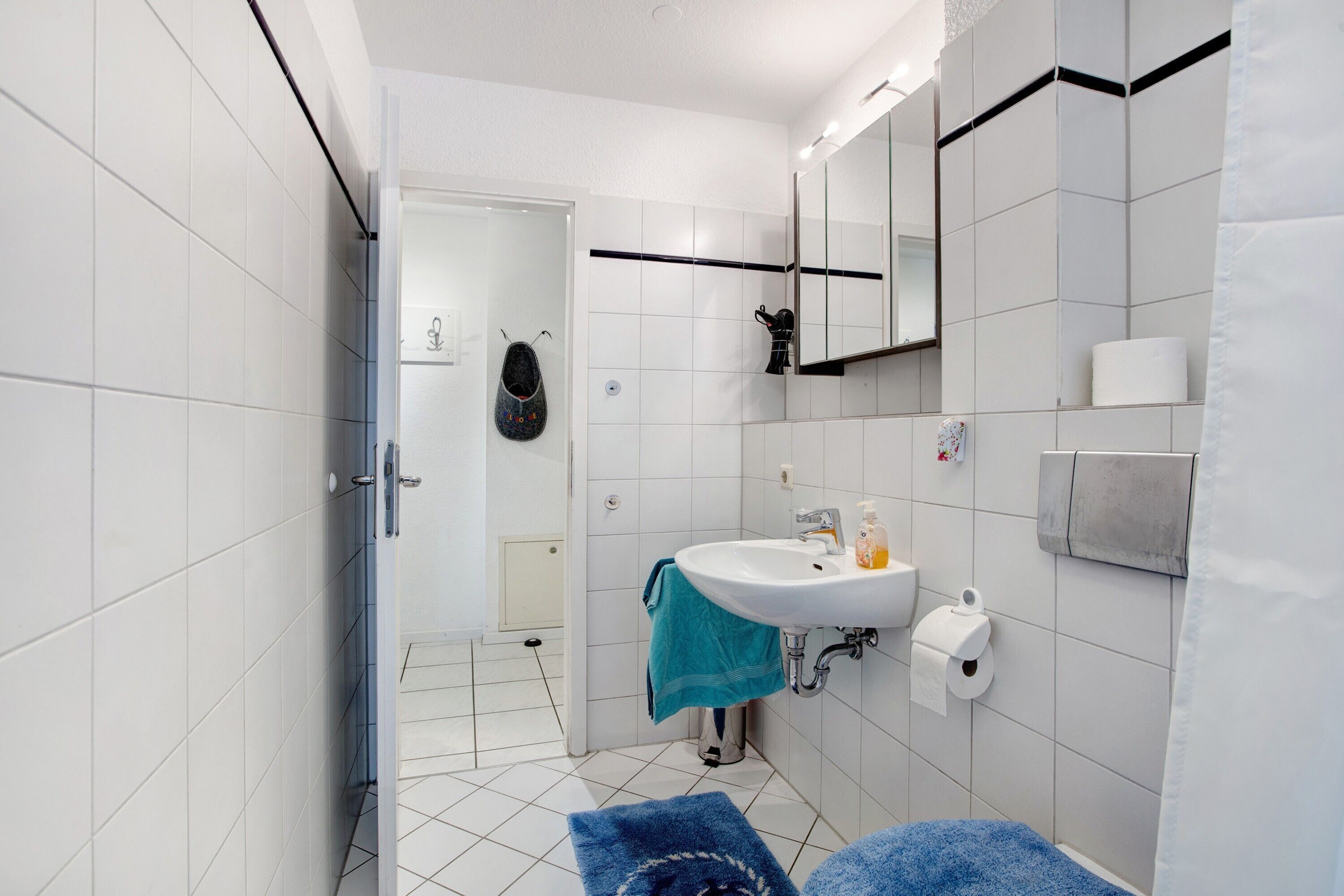 A modern bathroom with white tiles, a sink, a mirror, and a shower area.