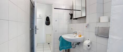 A modern bathroom with white tiles, a sink, a mirror, and a shower area.