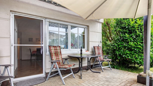 An outdoor patio with a table and two chairs, a sliding glass door leading to an interior room, and a green hedge in the background. - Apartment Ahorn with Private Terrace and Wi-Fi (Waldshut-Tiengen)