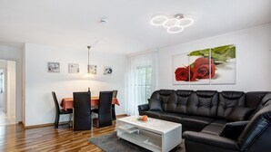 A modern living room with a black leather sofa, a white coffee table, a dining table with chairs, and a wall-mounted artwork of red roses. - Apartment Ahorn with Private Terrace and Wi-Fi (Waldshut-Tiengen)