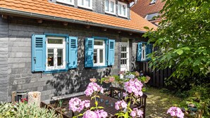 A stone house with blue shutters, a wooden bench, and pink flowers in the garden.