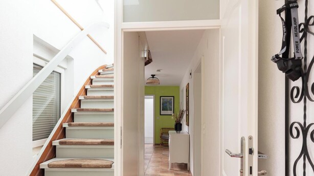 Un escalier dont les marches sont recouvertes de moquette, menant à une pièce dont un mur est peint en vert et qui possède une porte ornée d’une poignée décorative.