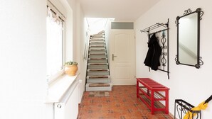 Un escalier menant à une porte, un banc rouge, un miroir fixé au mur et une plante en pot.