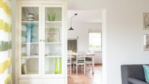 Une pièce comprenant un coin repas, un meuble blanc aux portes vitrées et un canapé gris.
