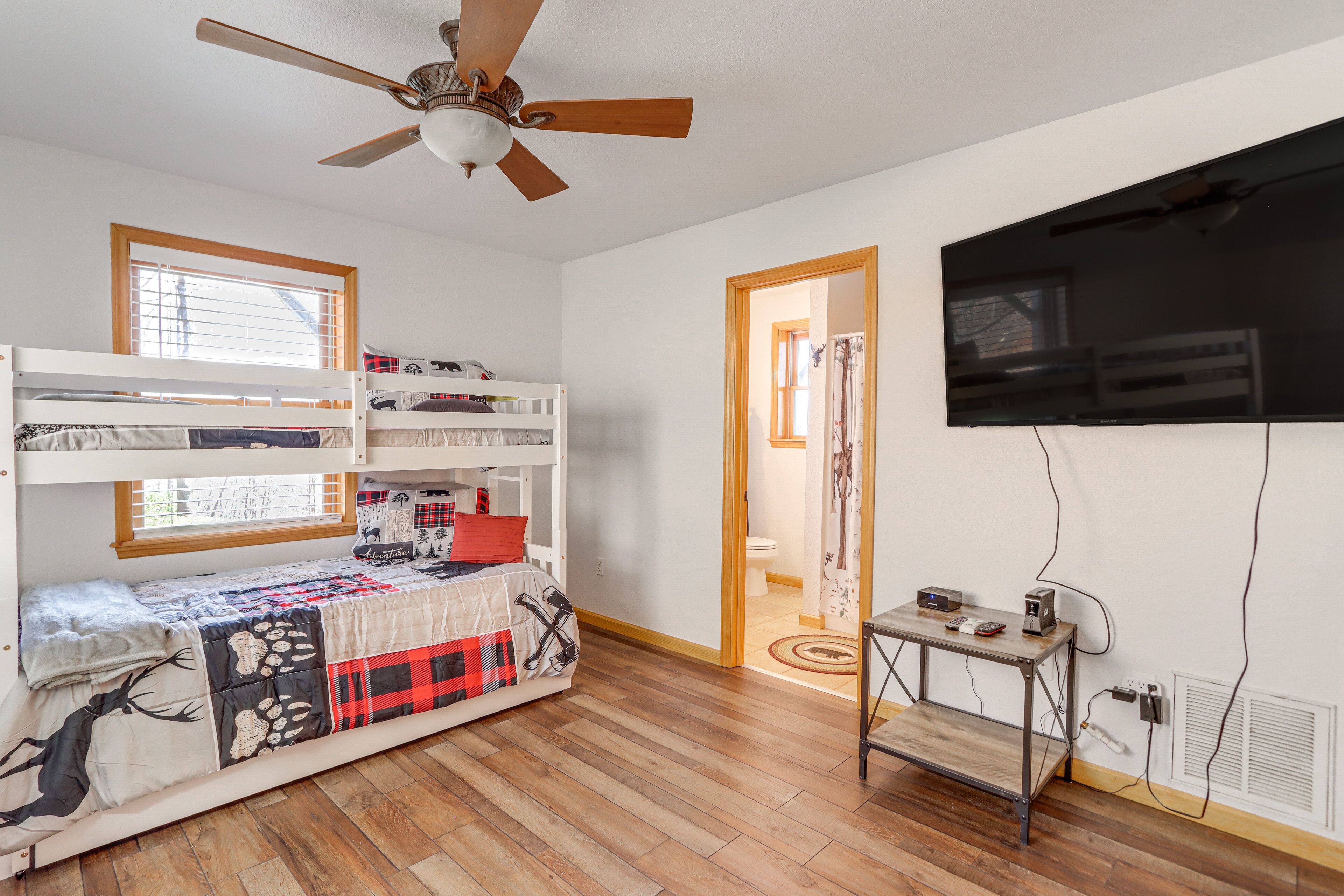 A room with bunk beds, a ceiling fan, a TV, and a small table with a power outlet.