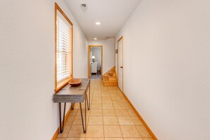 A narrow hallway with a wooden table and chairs, a window with blinds, and a door at the end.