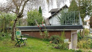 Ein Wohnhaus mit Garten, einer Holzbank, einem kleinen Schuppen und einem Balkon.