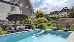A swimming pool with steps leading into it, surrounded by a garden with a sofa and an umbrella. - Apartment "Kebben" with Shared Terrace, Garden, and Pool (Kirchhundem)
