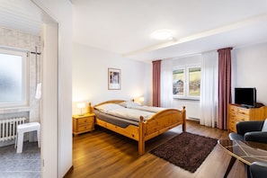Een slaapkamer met een houten bed, nachtkastjes, een televisie, een raam met gordijnen en een radiator.