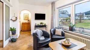 A modern living room with a fireplace, a television, and a view of the outdoors. - Apartment "Kebben" with Shared Terrace, Garden, and Pool (Kirchhundem)