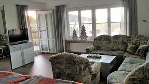 Ein Wohnzimmer mit einer Couch, einem Couchtisch, einem Fernseher und einem Fenster mit Vorhängen.