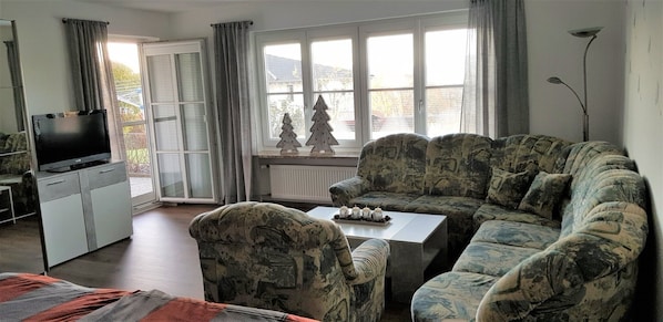 A living room with a sofa, a coffee table, a TV, and a window with curtains.