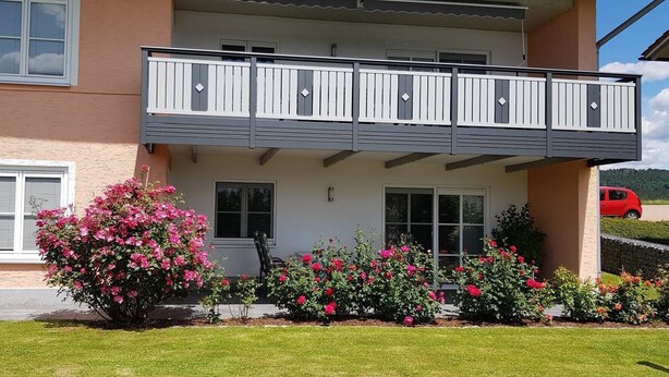 Ein zweistöckiges Haus mit Balkon und Rasen, im Hintergrund ein rotes Auto.