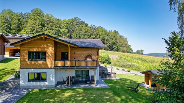 A two-story wooden house with a balcony, a lawn, and a view of a field. - Chalet 'Landhaus Rachelblick' with Mountain View, Private Terrace and Wi-Fi (Eppenschlag)