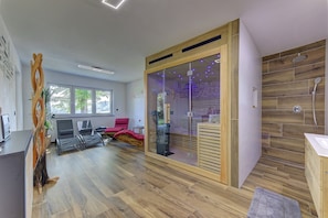 A modern room with a wooden floor, a glass partition, a shower area, and a seating area with chairs.