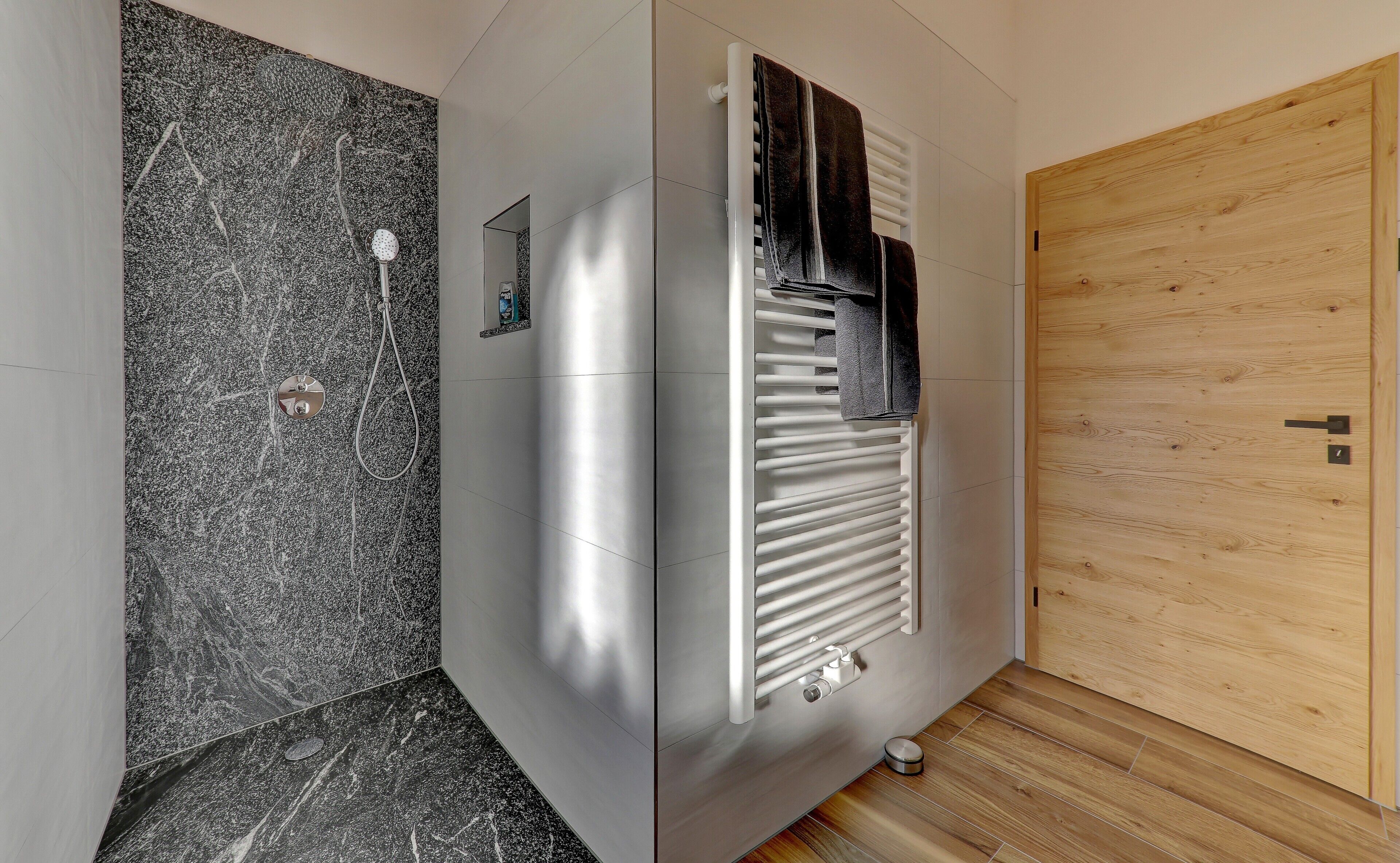 Une salle de bain avec une douche, un porte-serviettes et une porte en bois.