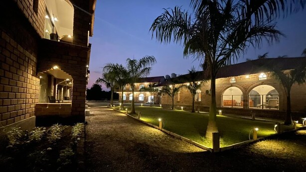 Un cortile ben illuminato con piscina, palme e un edificio con finestre ad arco e facciata in mattoni.