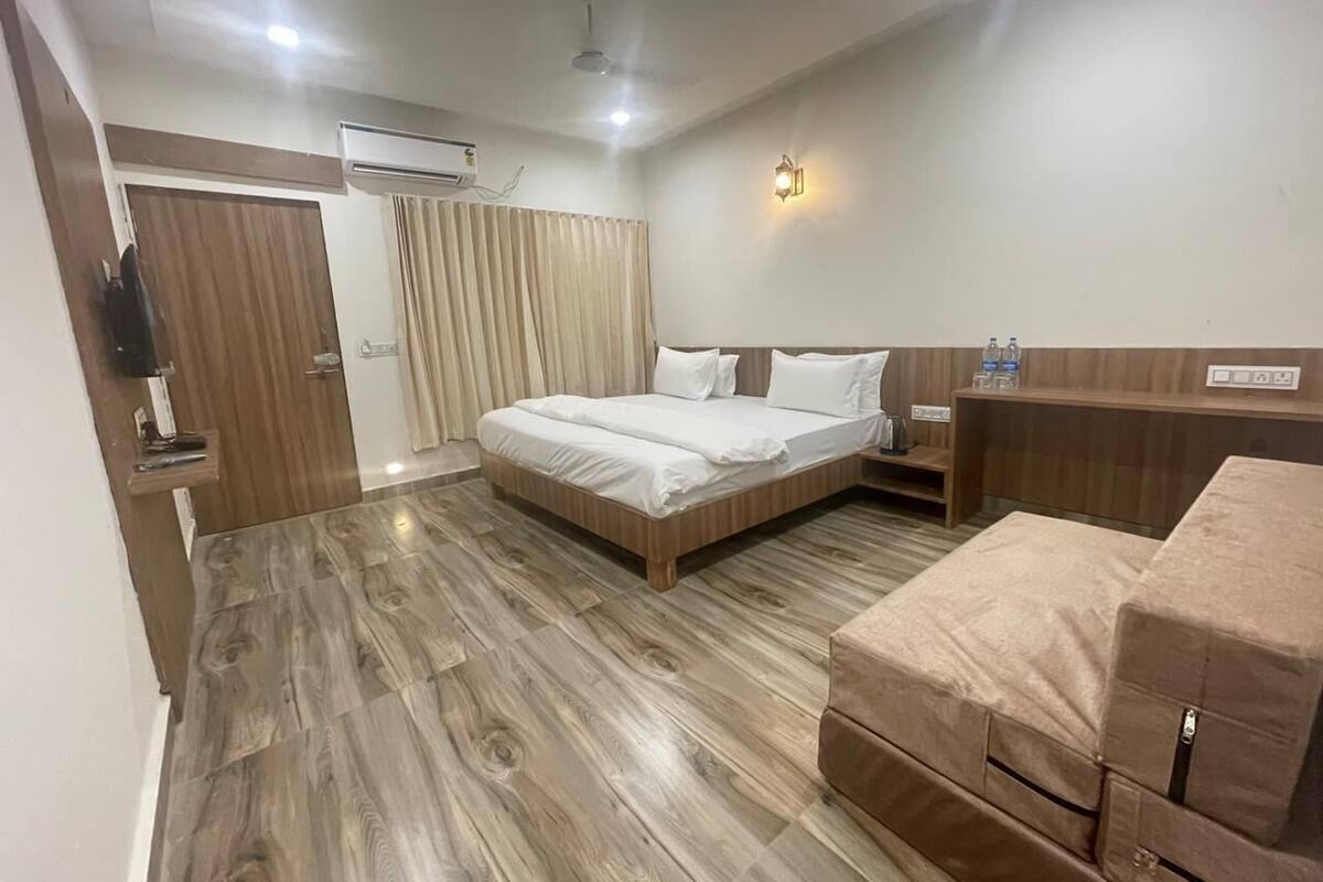 A hotel room with a wooden floor, a bed with white bedding, a wooden nightstand, a small table, and a wall-mounted TV.