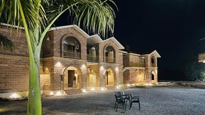 Un edificio in mattoni con diversi archi e balconi, un cortile in ghiaia e posti a sedere all'aperto.