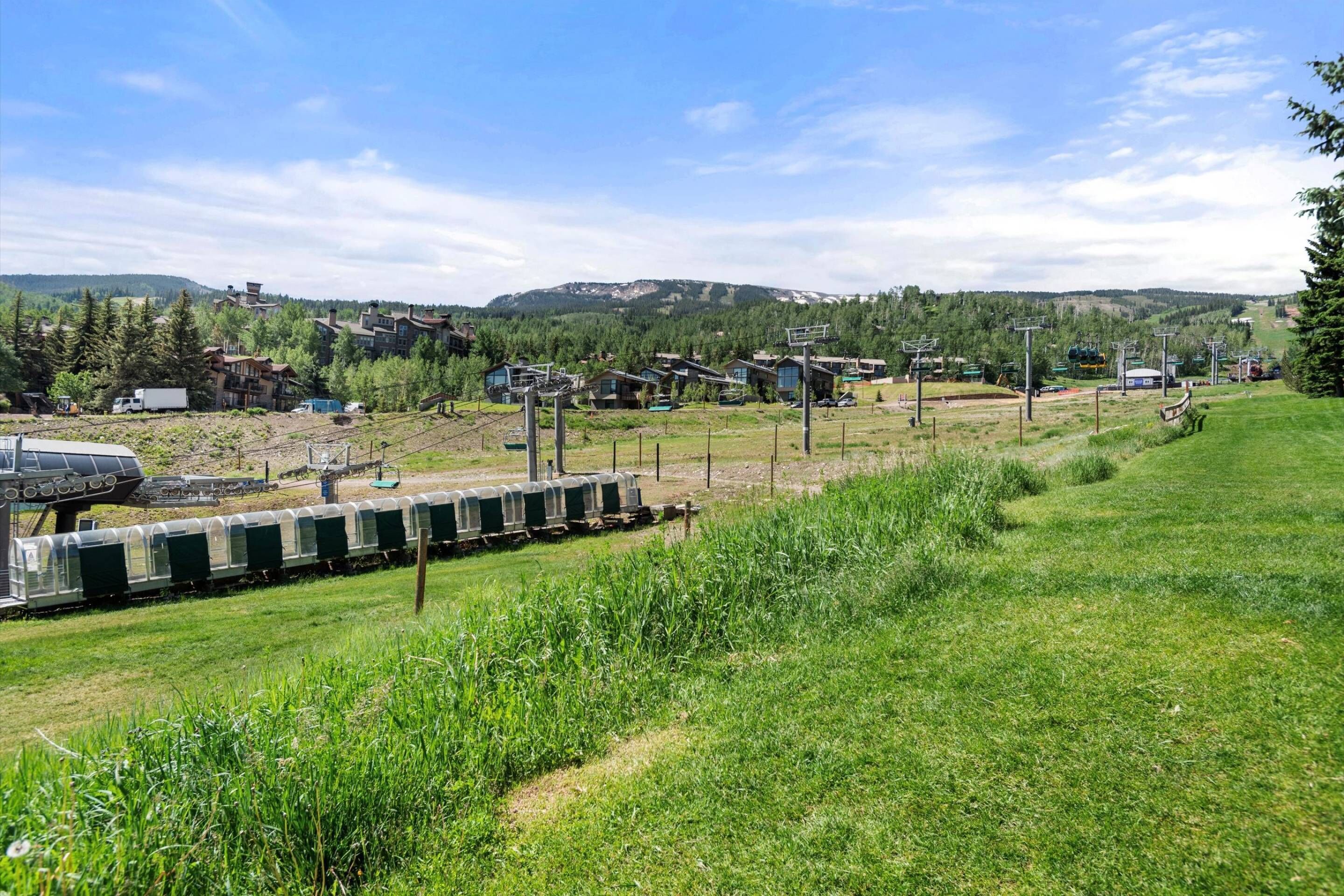 A train track with a stationary train, surrounded by green fields and residential buildings in a hilly area.