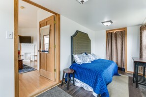 A bedroom with a bed, a wooden door, a small stool, a table, and a ceiling light fixture.