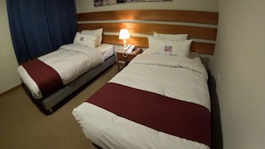Habitación de hotel con dos camas, una mesita de noche con lámpara y un cuadro de un paisaje urbano colgado en la pared.