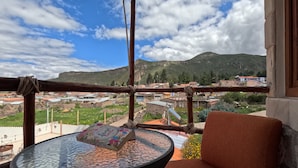 Un balcón con una mesa de vidrio, una silla acolchada y vistas a un pueblo con montañas al fondo.
