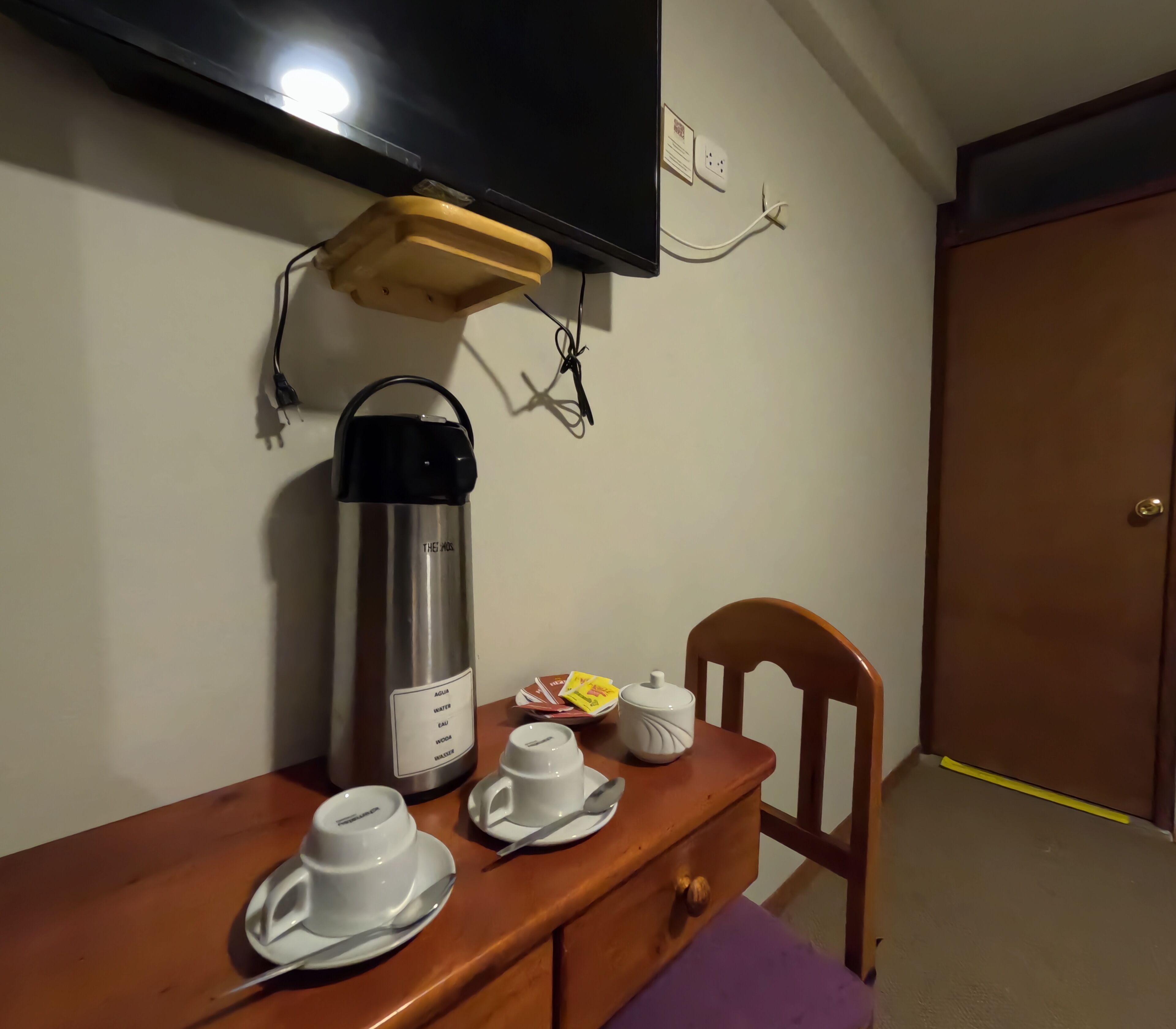 Una pequeña kitchenette con cafetera, tazas y tetera sobre una mesa de madera.