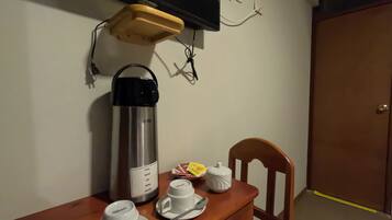 Una pequeña kitchenette con cafetera, tazas y tetera sobre una mesa de madera.