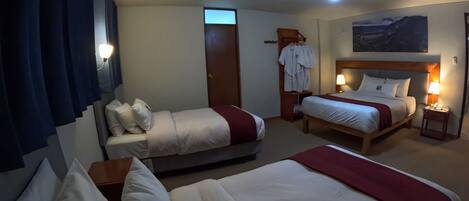 A hotel room with two beds, a robe rack, a desk, and a painting on the wall.
