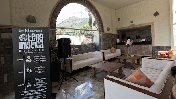 Vestíbulo de hotel con pared de piedra, un gran letrero, chimenea y un área de descanso con sofás y una mesita de centro.