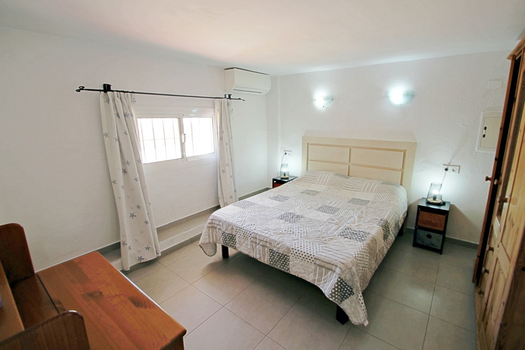 Une chambre à coucher avec un lit, une table de chevet, un bureau et une fenêtre avec des rideaux.