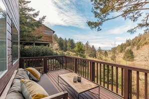 Eine Holzterrasse mit Bank und Tisch, mit Blick auf einen bewaldeten Hang.