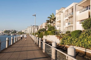 Um calçadão à beira-mar com edifícios modernos, céu claro e um corpo d'água calmo.