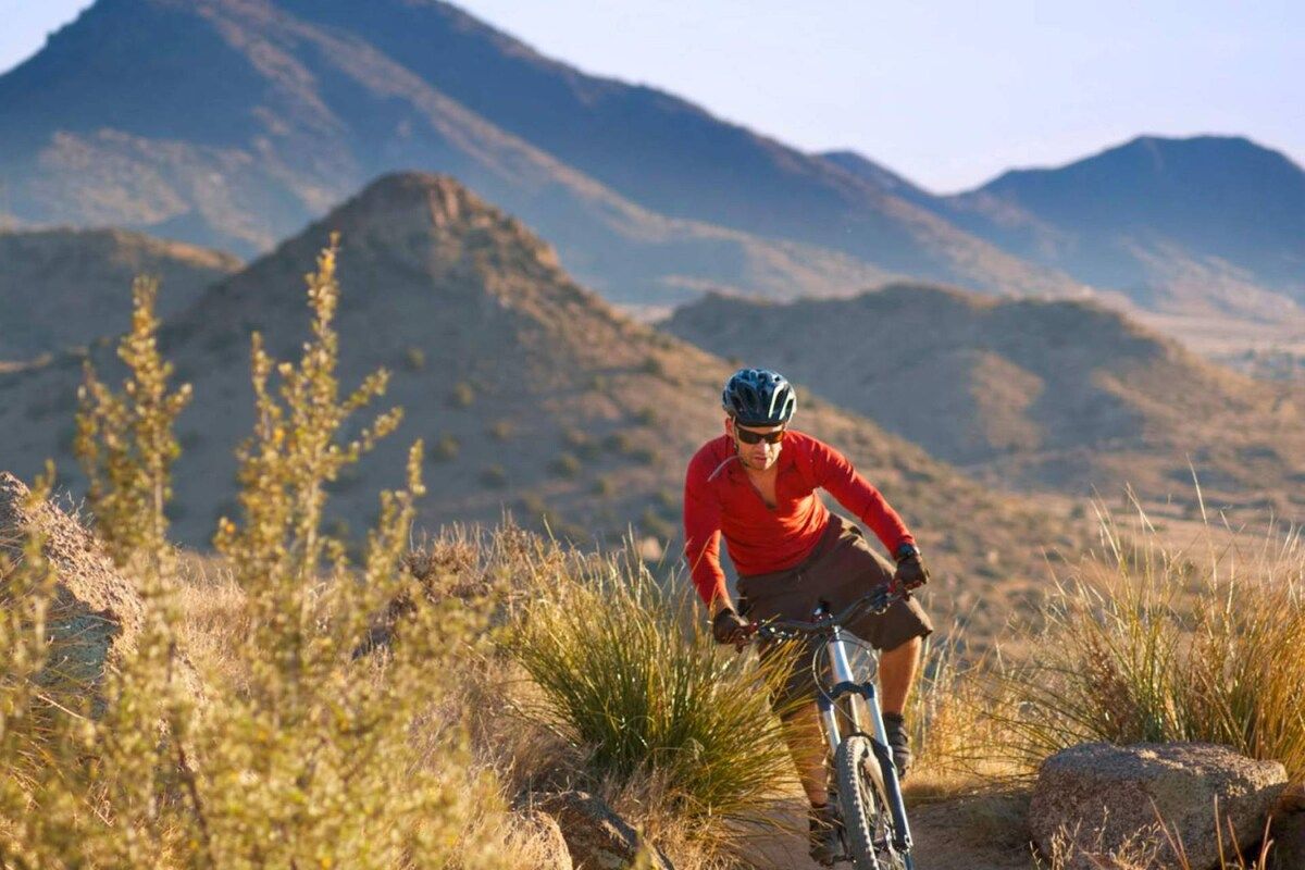 A person riding a mountain bike on a trail with a mountainous backdrop.
