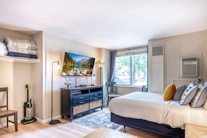 A bedroom with a bed, a TV, a desk, and a window.