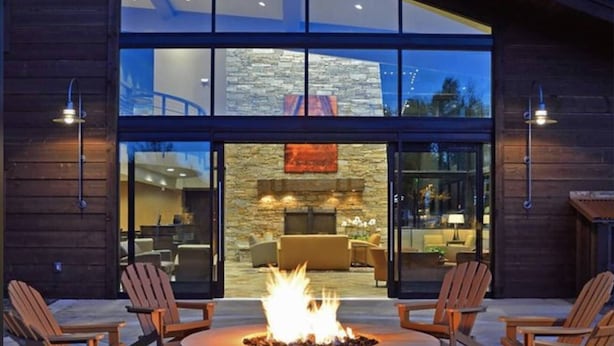 Un edificio moderno con fachada de piedra, amplios ventanales de vidrio y una chimenea en la zona de estar al aire libre.
