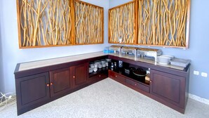 A modern kitchen with a built-in bar area, featuring a granite countertop, dark cabinetry, and a decorative wooden wall panel. - Flamingo Ceria (Labuan Bajo)