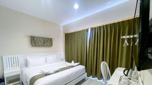 A modern hotel room with a neatly made bed, a bedside table, a chair, and a desk with a mirror and toiletries. - Flamingo Ceria (Labuan Bajo)