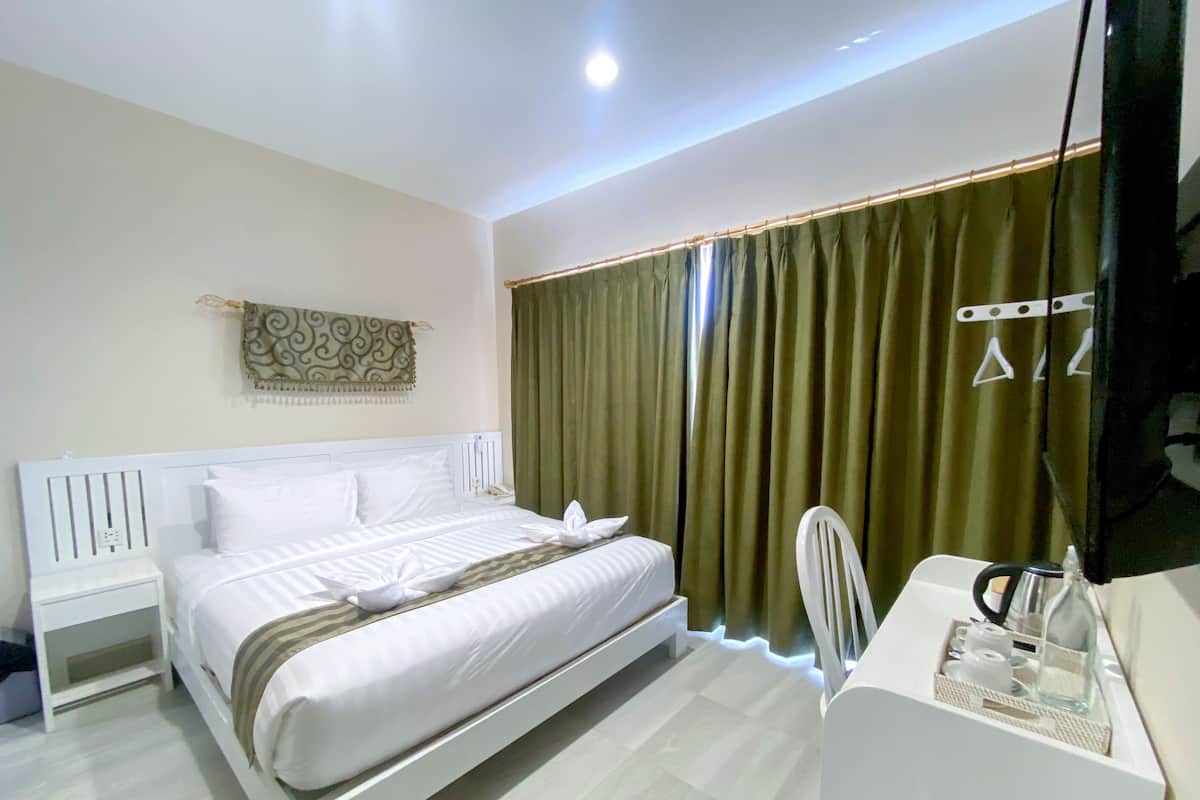 A modern hotel room with a neatly made bed, a bedside table, a chair, and a desk with a mirror and toiletries.