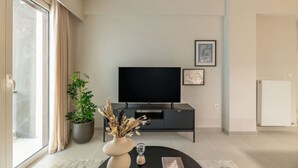 Una sala de estar moderna con un televisor de pantalla plana, una planta en maceta y un florero sobre una mesa de centro redonda.