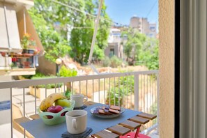 A balcony with a table set for breakfast, including fruits, a mug, and pastries.